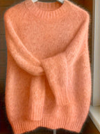 Pink sweater on a hanger against a wooden background