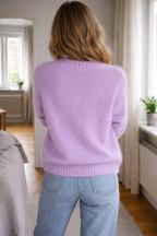 Person wearing a light purple sweater and blue jeans standing in a room with wooden floors and white walls.