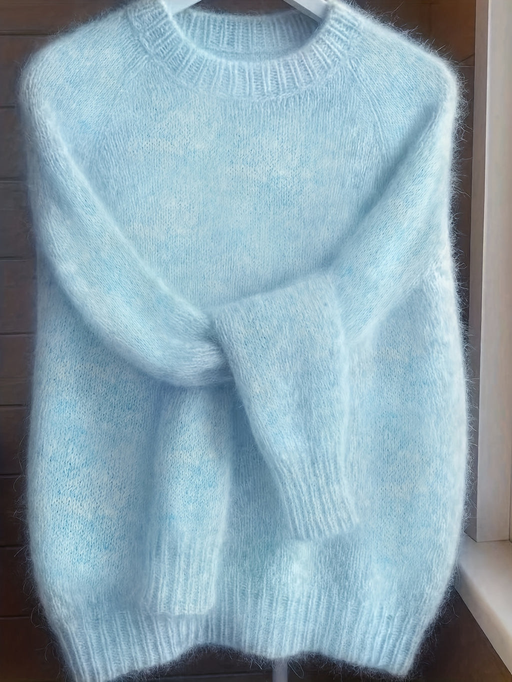 Light blue sweater on a hanger against a wooden background