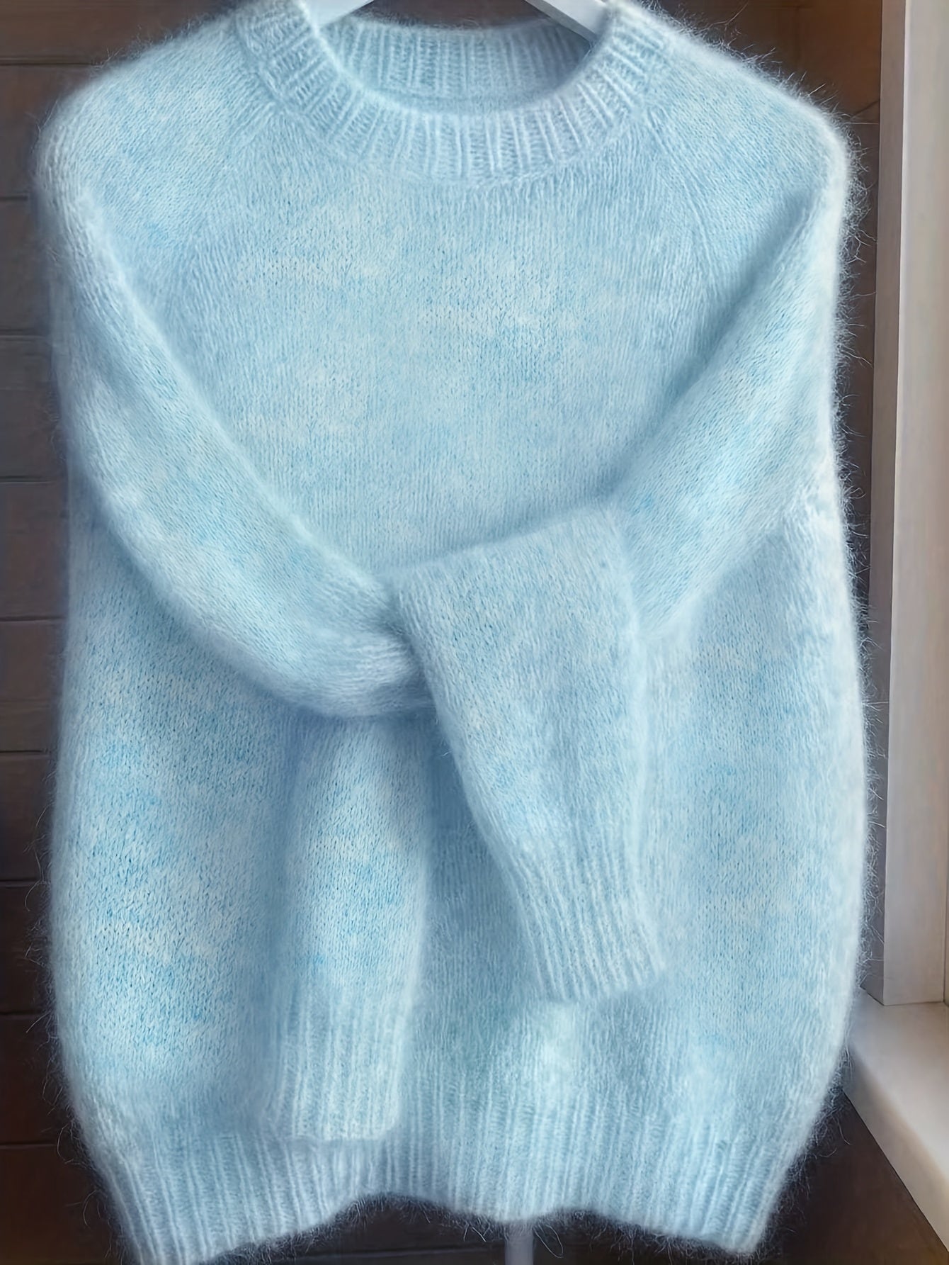 Light blue sweater on a hanger against a wooden background
