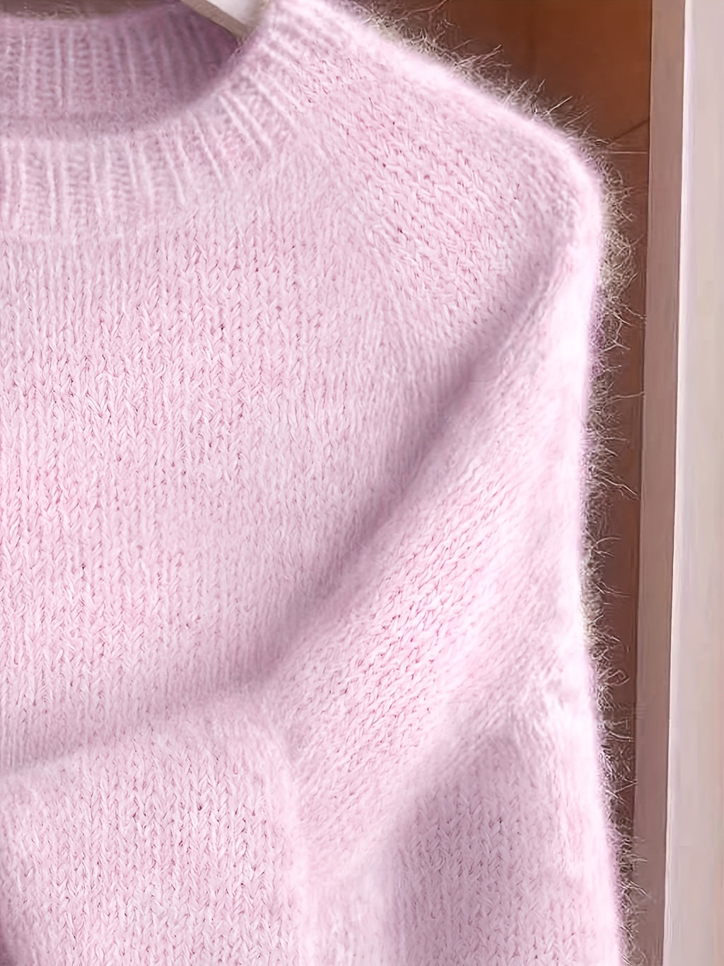 Close-up of a pink knitted sweater on a hanger.