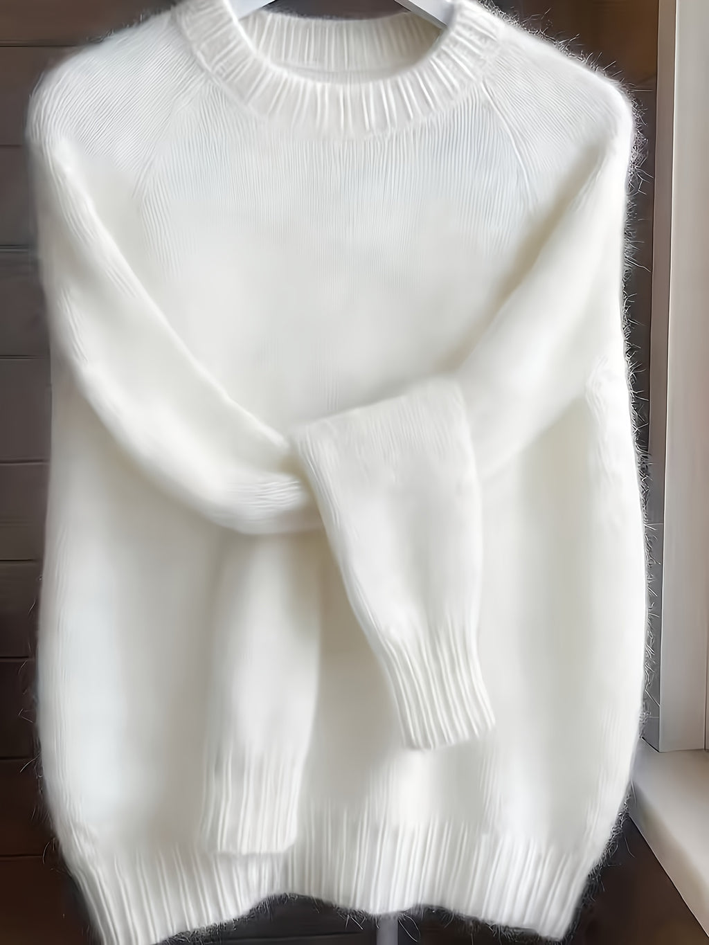 White sweater on a hanger against a wooden background
