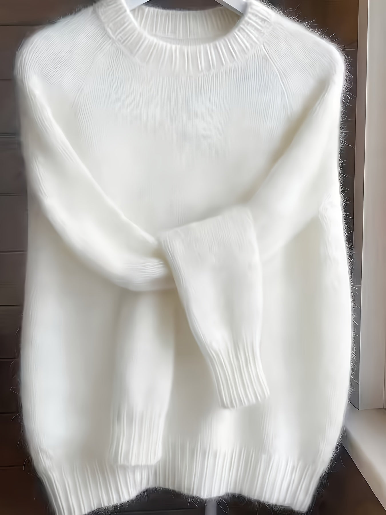 White sweater on a hanger against a wooden background