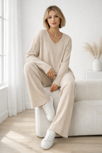 Woman in a beige ribbed sweater and pants sitting on a white couch in a bright room.