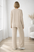 Person wearing a beige ribbed knit outfit in a bright room with white walls and wooden floor.