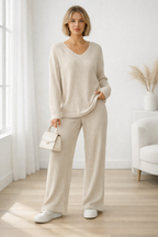 Woman wearing a beige ribbed sweater and pants in a minimalistic room.