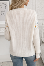 Woman wearing a cream knitted sweater with floral details in a minimalistic room.
