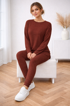 Woman in a brown ribbed outfit sitting on a white stool in a room with wooden flooring.