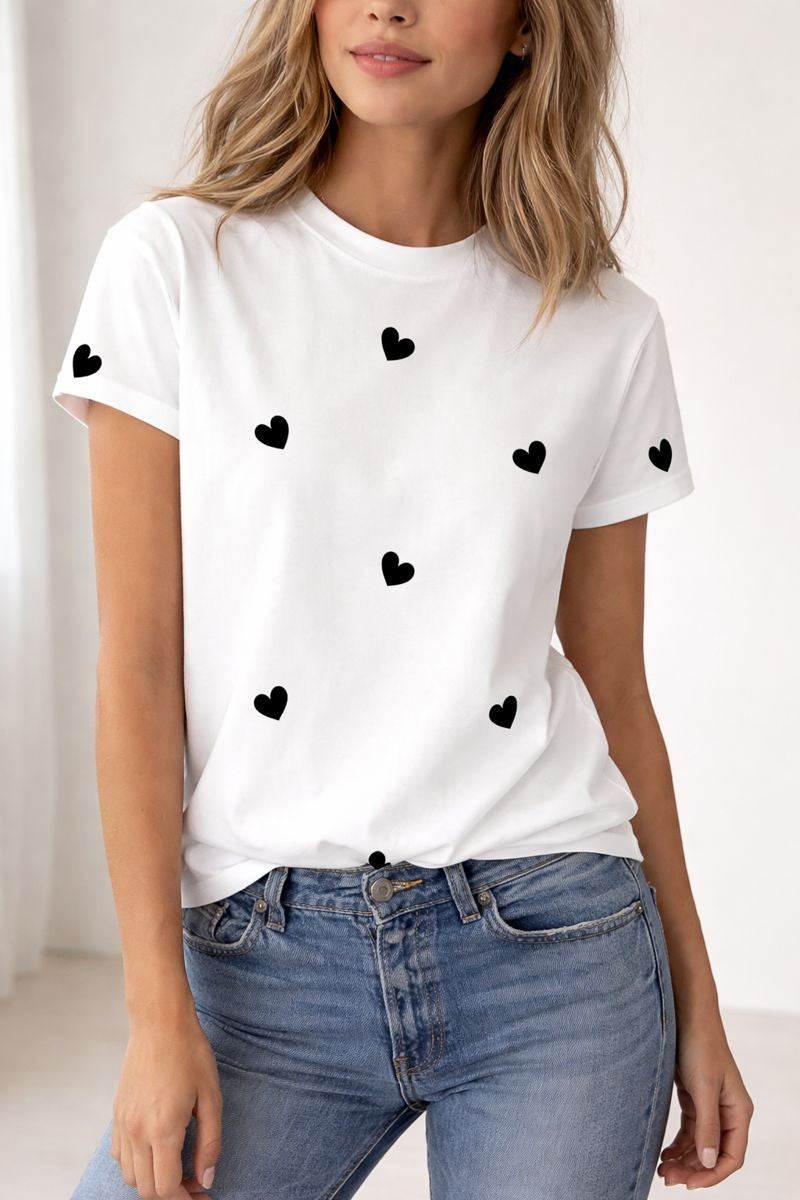 White t-shirt with black heart patterns worn by a person, paired with blue jeans on a white background