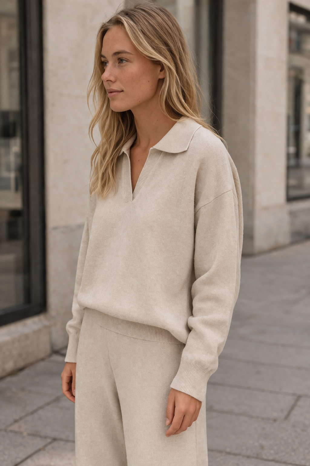 Woman wearing a beige sweater and pants standing on a street.