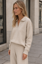 Woman wearing a beige sweater and pants standing on a street.