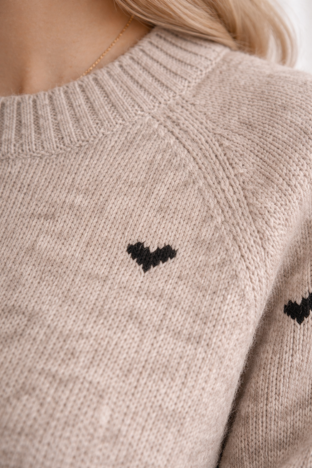 Close-up of a beige sweater with black heart patterns on the sleeves.