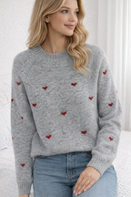 Woman wearing a gray sweater with red heart patterns against a white background