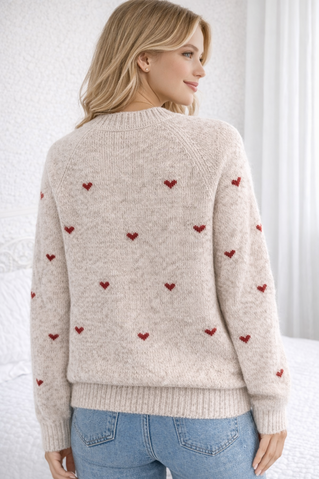 Woman wearing a beige sweater with red heart patterns against a white background