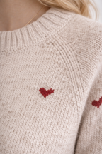 Beige sweater with red heart patterns on a neutral background