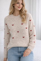Woman wearing a beige sweater with red heart patterns and blue jeans indoors.
