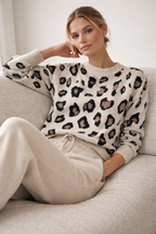 Woman wearing a leopard print sweater and beige pants sitting on a couch.