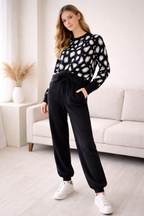 Woman wearing a black and white patterned sweater and black pants in a living room.