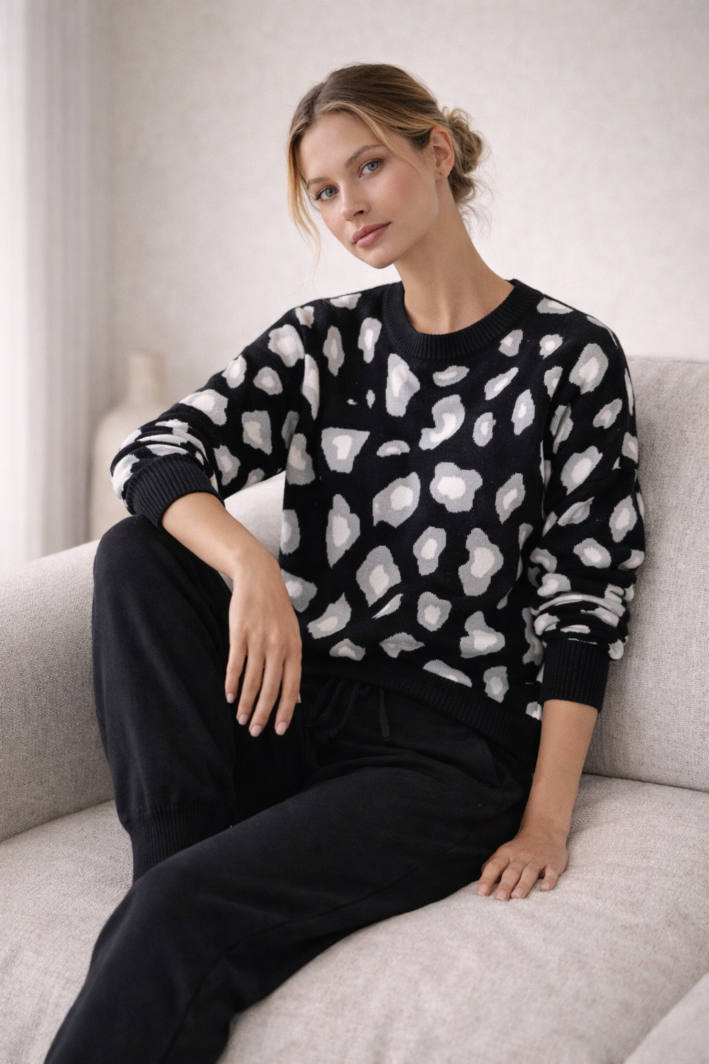 Woman wearing a black sweater with white abstract patterns sitting on a light gray couch.