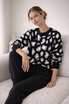 Woman wearing a black sweater with white abstract patterns sitting on a light gray couch.