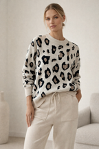 Woman wearing a leopard print sweater and beige pants in a neutral setting