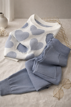 White sweater with blue heart patterns and matching pants on a light surface.