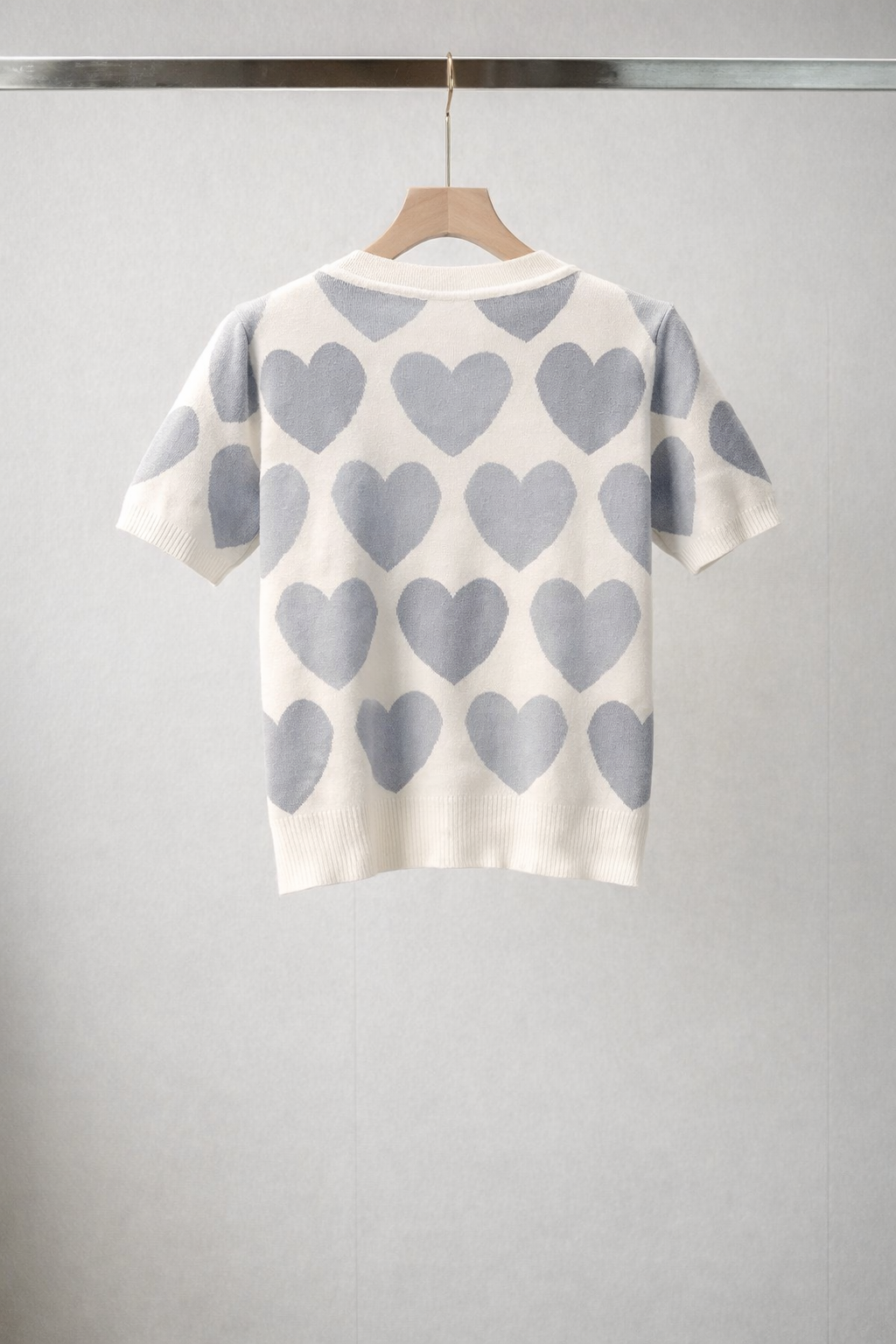 White sweater with gray hearts on a hanger against a gray background
