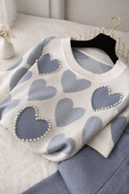 White sweater with blue heart patterns and pearl details on a hanger.