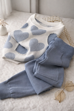White sweater with blue heart patterns and matching pants on a light surface.