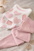 Pink heart-patterned sweater and pants set on a neutral background
