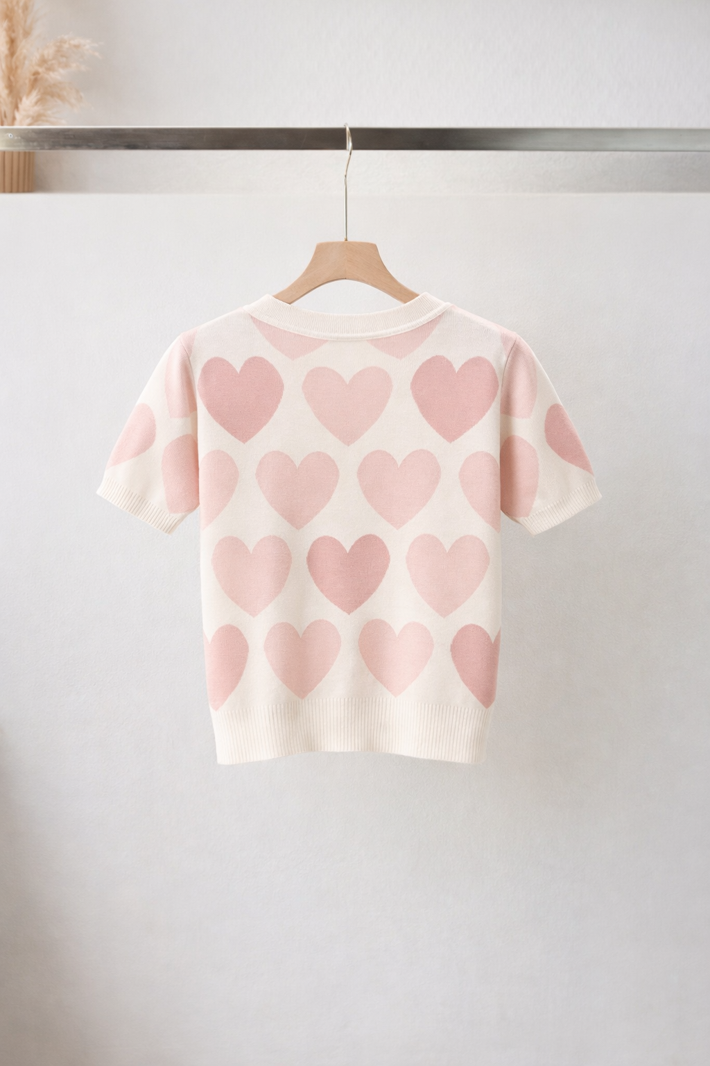 White t-shirt with pink heart patterns hanging on a rack against a white background