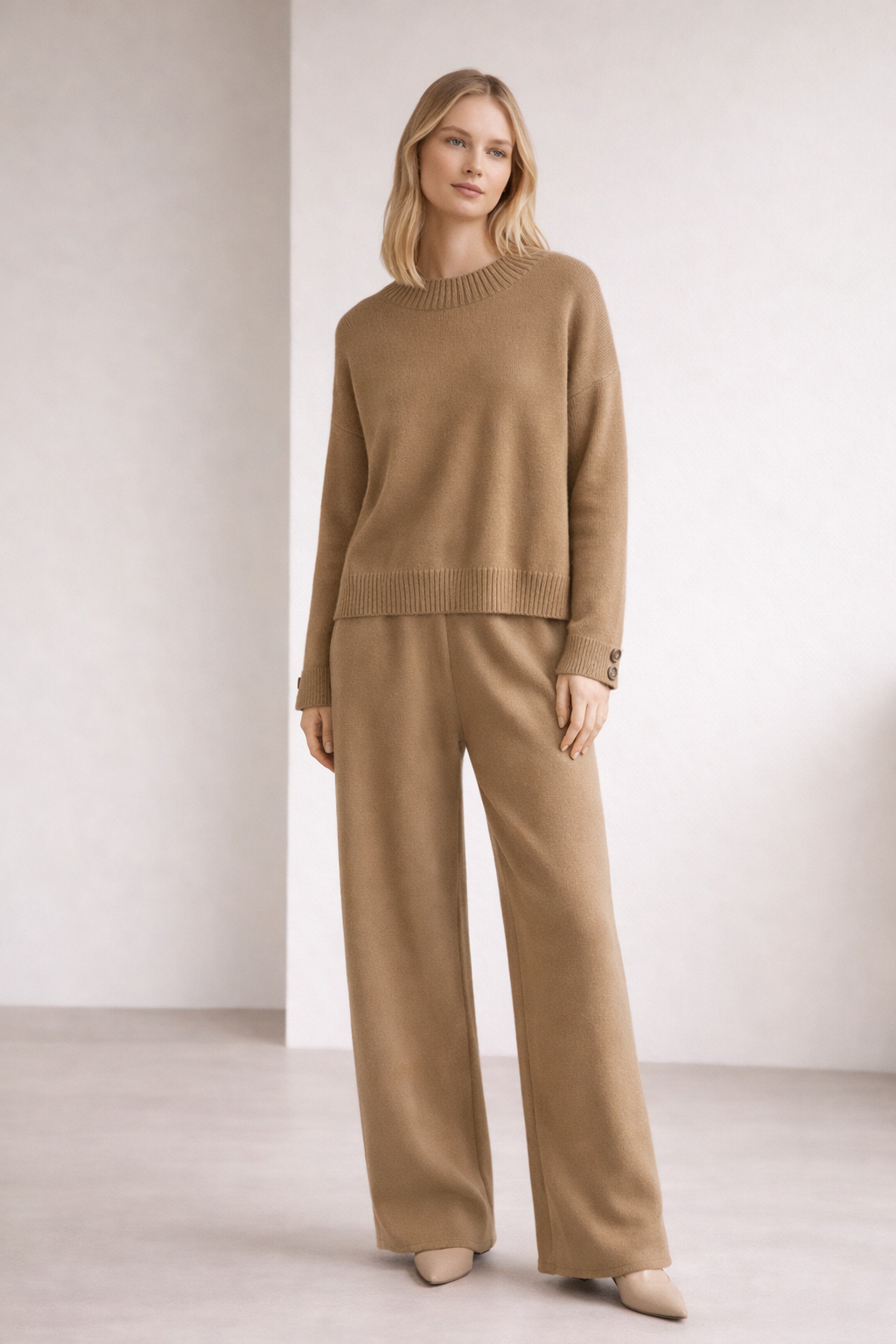 Woman wearing a beige sweater and pants set against a plain background