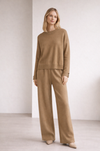 Woman wearing a beige sweater and pants set against a plain background