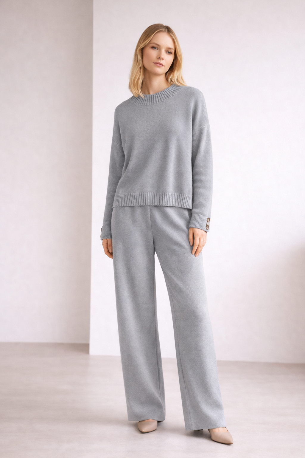 Woman wearing a light gray sweater and pants set against a white background