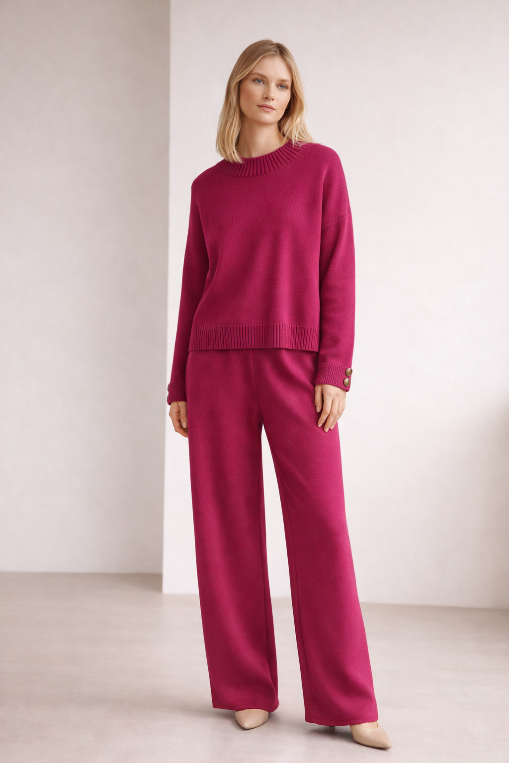 Woman wearing a magenta outfit with a matching sweater and pants against a plain background