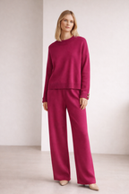 Woman wearing a magenta outfit with a matching sweater and pants against a plain background