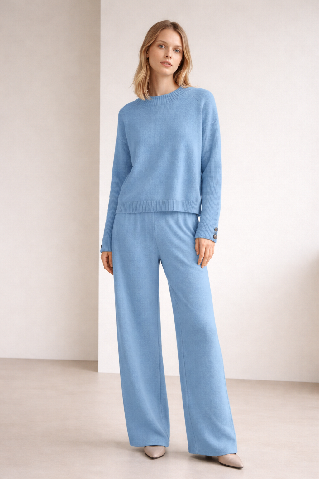 Woman wearing a light blue outfit with a sweater and pants on a plain background