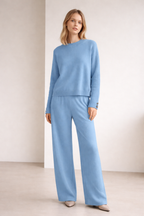 Woman wearing a light blue outfit with a sweater and pants on a plain background