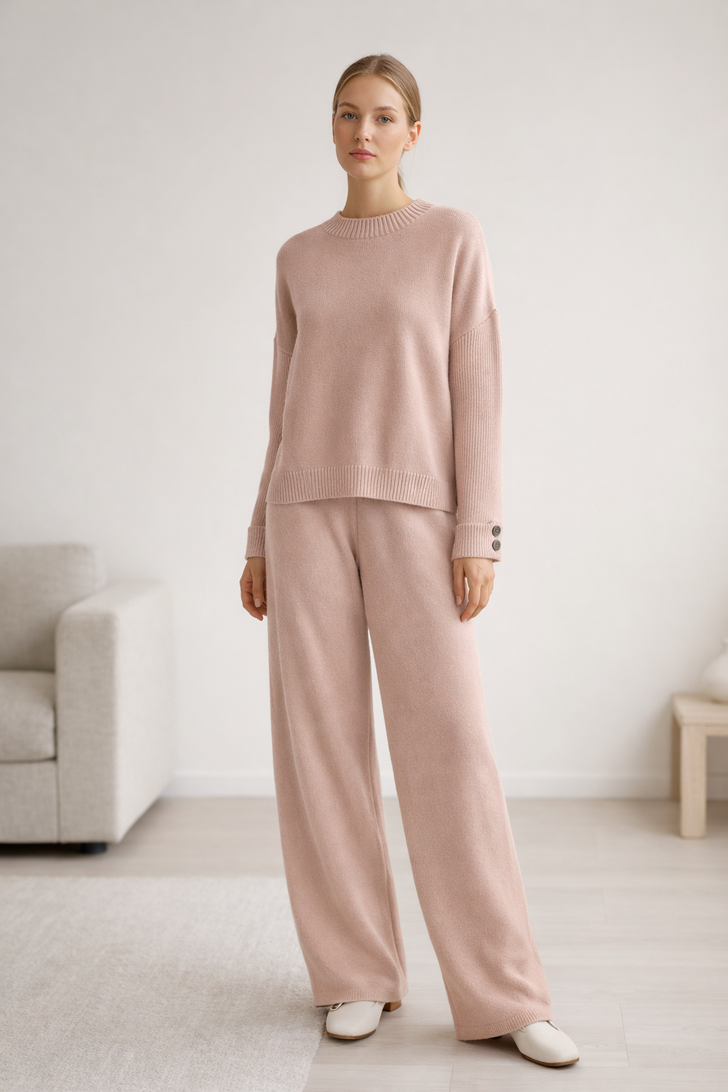 Woman wearing a pink sweater and pants in a minimalistic room.