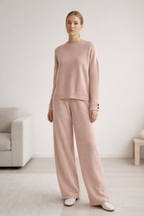 Woman wearing a pink sweater and pants in a minimalistic room.