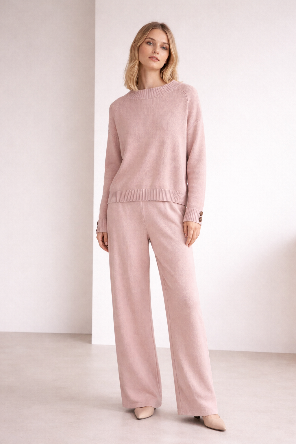 Woman wearing a pink sweater and pants against a white background