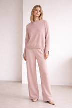 Woman wearing a pink sweater and pants against a white background