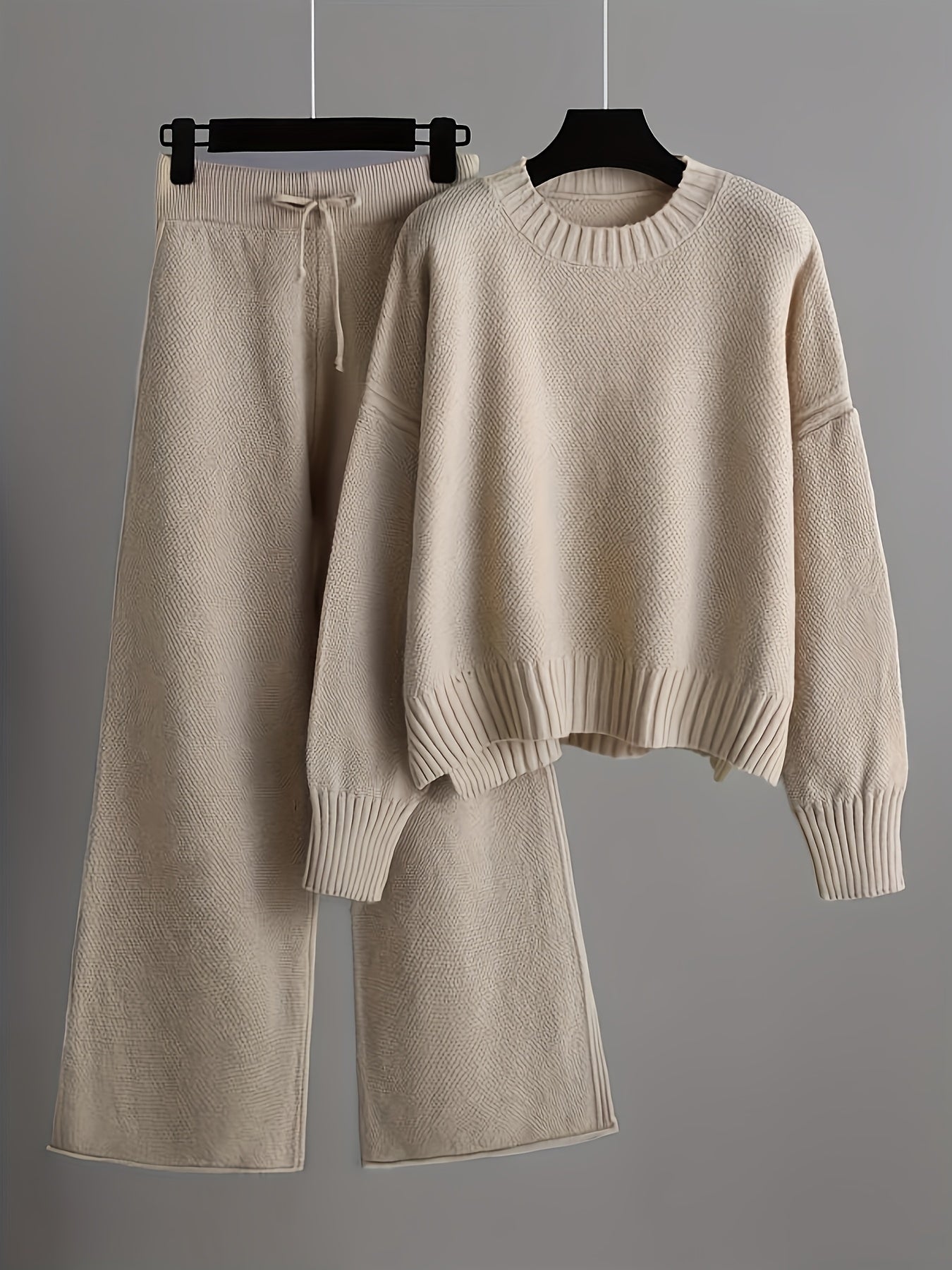 Beige sweater and pants set on hangers against a gray background