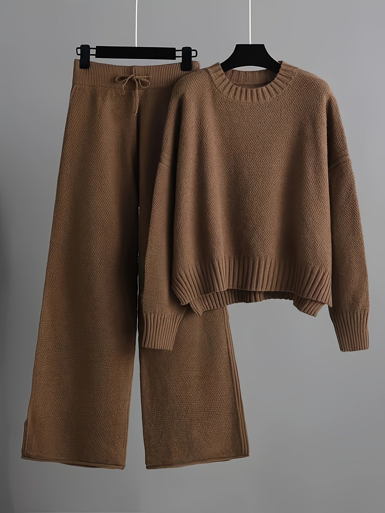 Brown knitted sweater and wide-leg pants set on hangers against a gray background