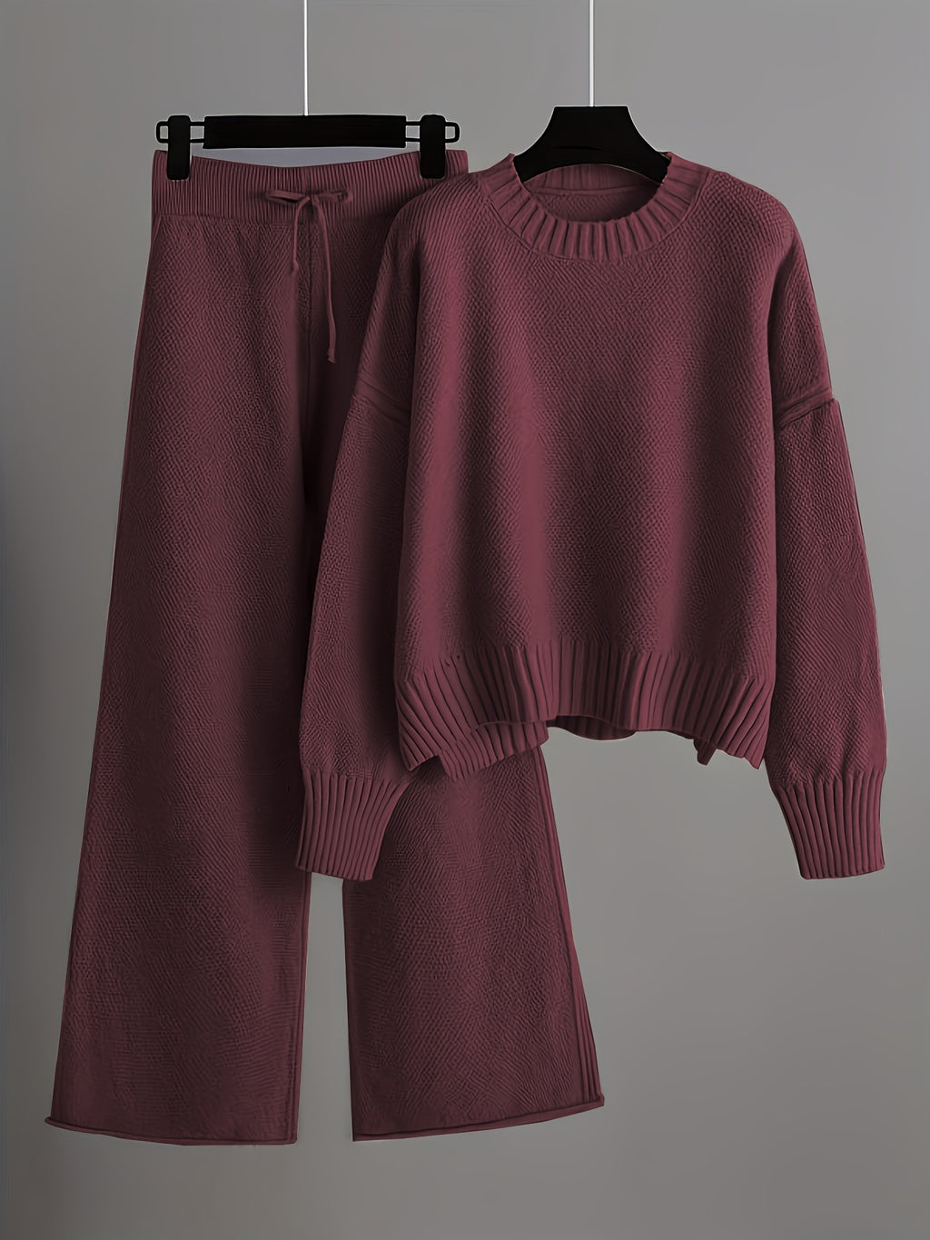 Maroon sweater and pants set on hangers against a gray background