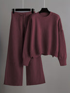 Maroon sweater and pants set on hangers against a gray background