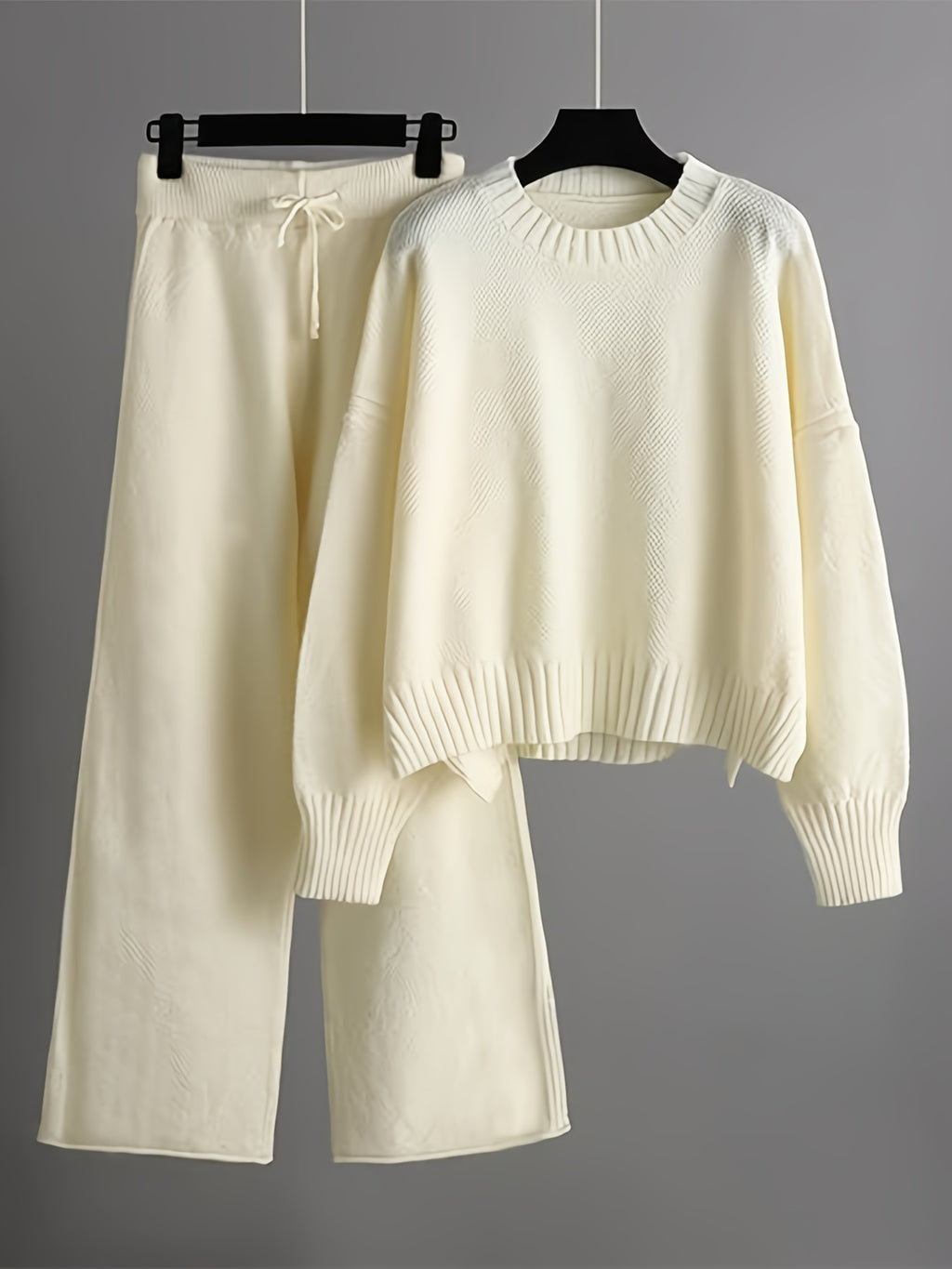 White sweater and pants set on hangers against a gray background