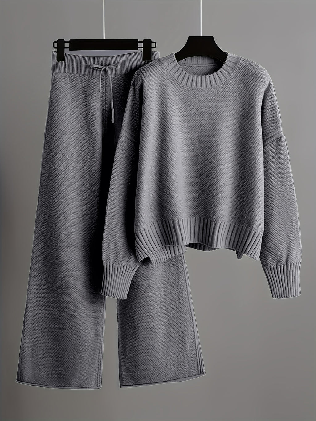 Gray sweater and wide-leg pants on hangers against a gray background