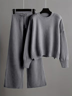 Gray sweater and wide-leg pants on hangers against a gray background