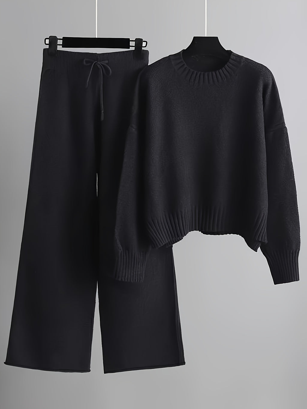 Black sweater and black pants on hangers against a gray background